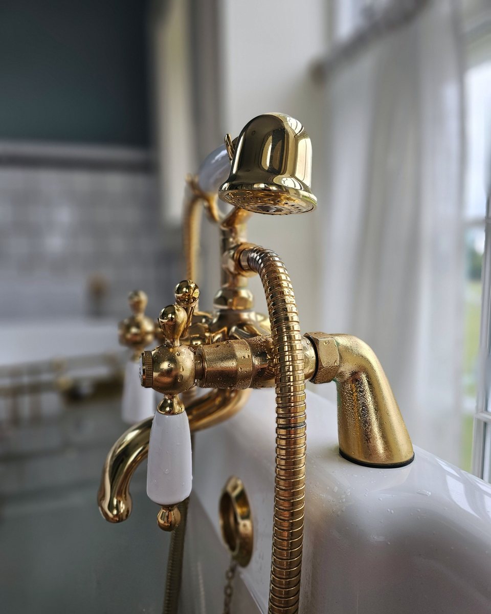 Brass bath taps with porcelain handles beside a sunlit window