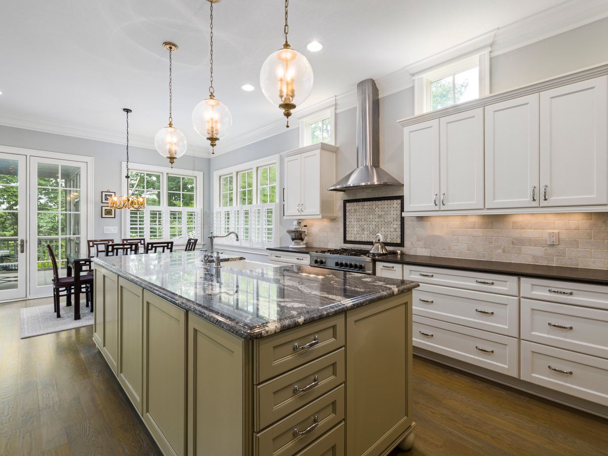 A sage green kitchen island with a granite worktop and glass pendant lights